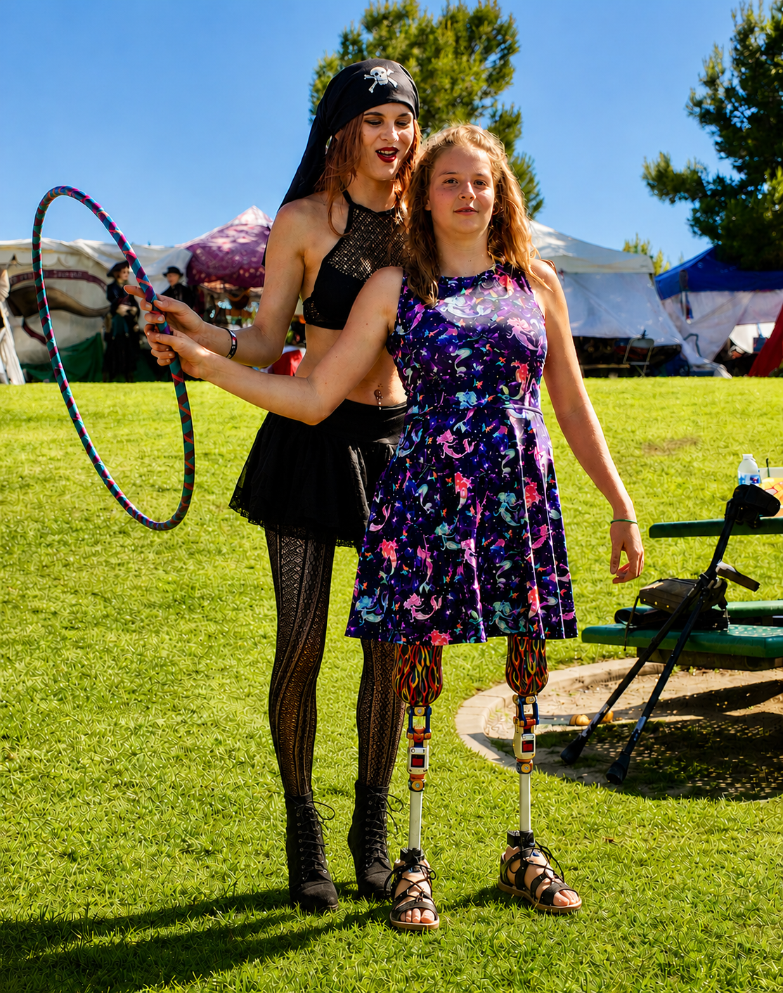 Sunshine Hoops pirate instructor teaching a young girl with prosthetic legs how to hoop at a festival