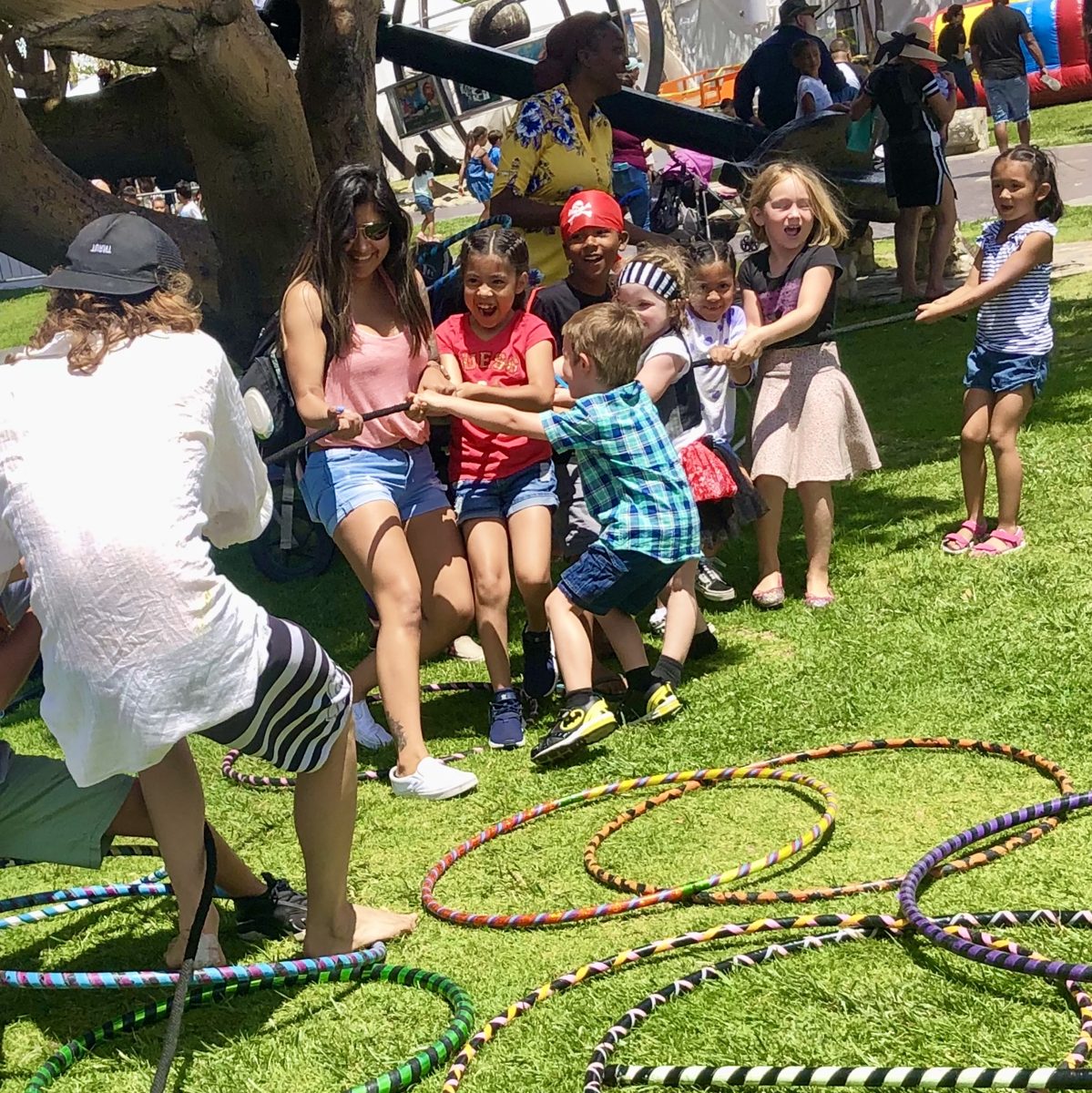 Laughing kids and adults playing tug-of-war surrounded by colorful hoops at a Sunshine Hoops event